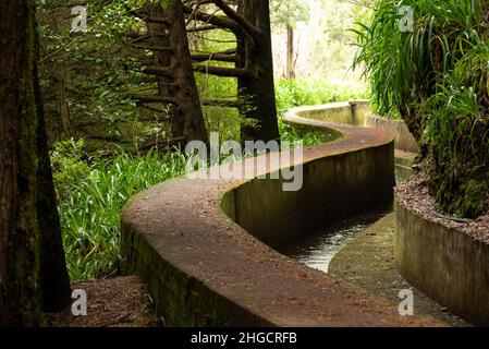 Gewundene Betonwand des Wasserkanals „Levada das Rabacas“ und Wanderweg, der am Bergpass „Boca da Encumeada“, Madeira, beginnt Stockfoto