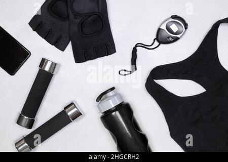 Sport-BH, Fitnesshandschuhe, digitale Stoppuhr, Kurzhanteln, Wasserflasche, Smartphone-Layout. Weibliches Sporttraining Trainingskonzept Stockfoto