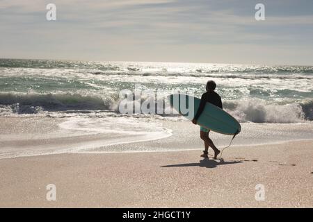 Die ganze Länge der Biracial Senior Mann mit Surfbrett zu Fuß in Richtung Wellen im Meer am Strand Stockfoto