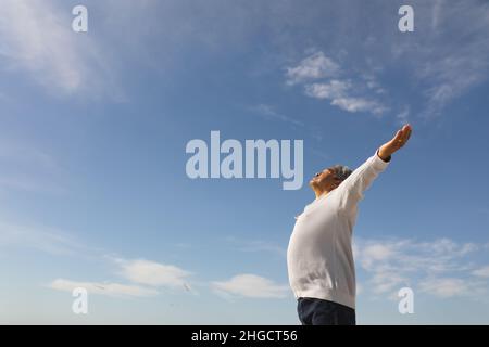 Low-Angle-Ansicht eines sorglosen Senioren aus der Biracial-Familie mit ausgestreckten Armen am sonnigen Tag vor dem blauen Himmel Stockfoto