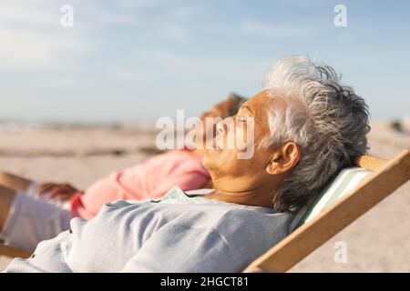 Seitenansicht einer älteren Frau, die mit einem Mann am Strand auf einem Stuhl schläft Stockfoto