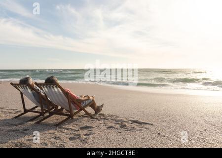 Ältere Männer und Frauen aus dem Biracial entspannen sich, während sie am Strand auf Klappstühlen sitzen Stockfoto