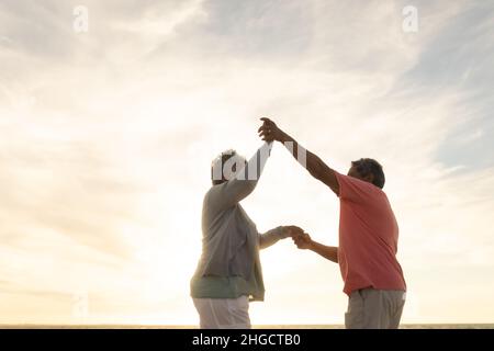 Low-Angle-Seitenansicht Senior multiracial Paar genießen Tanz am Strand gegen Himmel während des Sonnenuntergangs Stockfoto