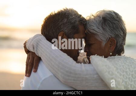 Seitenansicht des liebevollen jungen Biracial Senior Braut und Bräutigam umarmen während des Sonnenuntergangs Stockfoto