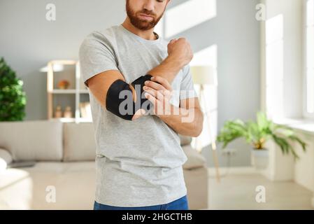 Der Mann trägt einen Verband am Ellbogen, der als Fixator dient, um Gelenkschmerzen wiederherzustellen und zu lindern. Stockfoto