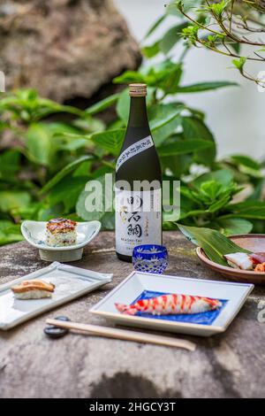 Sushi-Set und Sashimi mit Sake auf grauem Stein serviert mit Garten im Hintergrund. Stockfoto