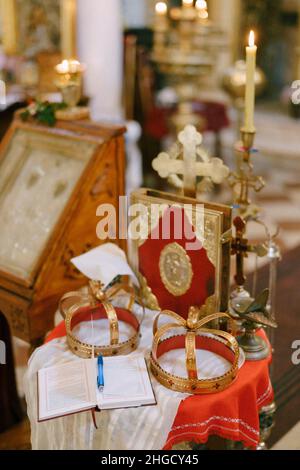 Kreuz, goldene Kronen, Bibel und Kerzenständer stehen auf dem Tisch in der Kirche Stockfoto