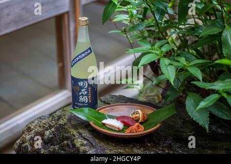 Sushi-Set und Sashimi mit Sake auf grauem Stein serviert mit Garten im Hintergrund. Stockfoto