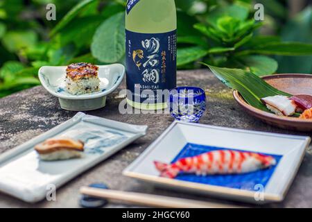 Sushi-Set und Sashimi mit Sake auf grauem Stein serviert mit Garten im Hintergrund. Stockfoto