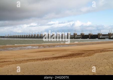 Blick über das Meer zur östlichen Schelde-Sturmflutbarriere in Zeeland mit stürmischem Himmel, dramatischem Sonnenlicht und Sandstrand im Vordergrund. Ooster Stockfoto