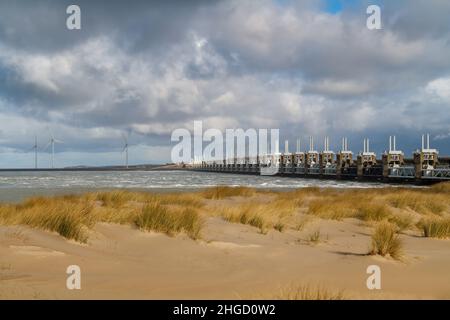 Blick über das Meer zur östlichen Schelde-Sturmflutbarriere in Zeeland mit stürmischem Himmel, dramatischem Sonnenlicht mit Sanddünen, Gras und Strand Stockfoto