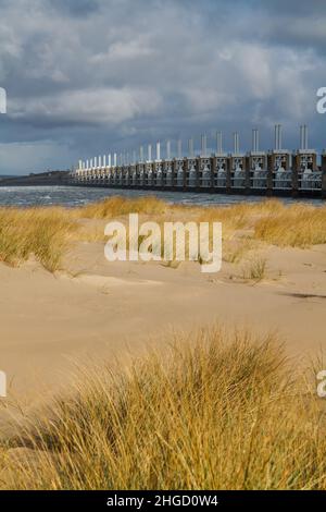 Blick über das Meer zur östlichen Schelde-Sturmflutbarriere in Zeeland mit stürmischem Himmel, dramatischem Sonnenlicht mit Sanddünen, Gras und Strand Stockfoto