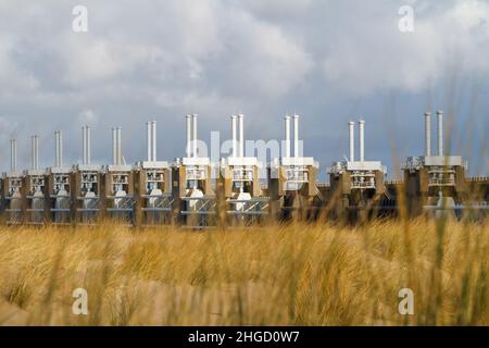 Blick über das Meer zur östlichen Schelde-Sturmflutbarriere in Zeeland mit stürmischem Himmel, dramatischem Sonnenlicht mit Sanddünen, Gras und Strand Stockfoto