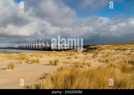 Blick über das Meer zur östlichen Schelde-Sturmflutbarriere in Zeeland mit stürmischem Himmel, dramatischem Sonnenlicht mit Sanddünen, Gras und Strand Stockfoto