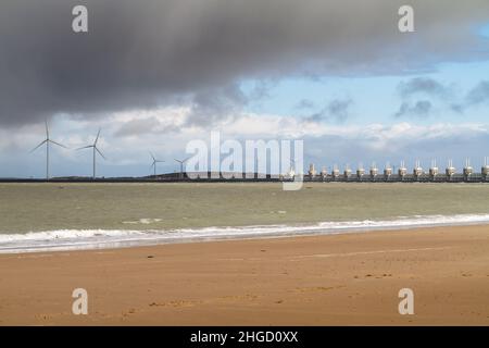 Blick über das Meer zur östlichen Schelde-Sturmflutbarriere in Zeeland mit stürmischem Himmel, dramatischem Sonnenlicht und Sandstrand im Vordergrund. Ooster Stockfoto