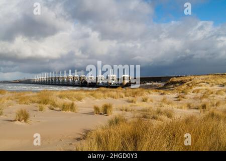 Blick über das Meer zur östlichen Schelde-Sturmflutbarriere in Zeeland mit stürmischem Himmel, dramatischem Sonnenlicht mit Sanddünen, Gras und Strand Stockfoto