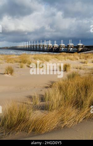 Blick über das Meer zur östlichen Schelde-Sturmflutbarriere in Zeeland mit stürmischem Himmel, dramatischem Sonnenlicht mit Sanddünen, Gras und Strand Stockfoto