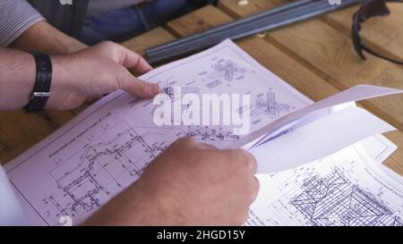 Nahaufnahme der Hände von Arbeitern in einer Fabrik, die technische Zeichnungen durchschauen. Baupläne mit Skizzen von Projekten, Engineering-Konzept Stockfoto