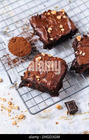 Schokoladen-Fudge-Brownies mit Haselnussbröseln oben, auf einem Tablett mit Kakaopulver, Schokoladenbröseln auf weißem, rustikalem Hintergrund. Stockfoto