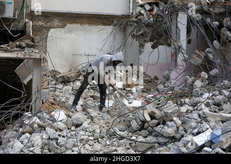 Arbeiter arbeiten daran, die Schutt zu entfernen das zerstörte Gebäude wurde durch Luftangriffe während des israelisch-palästinensischen Konflikts im vergangenen Jahr im Gazastreifen am 19. Januar 2022 zerstört. Stockfoto