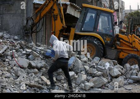 Arbeiter arbeiten daran, die Schutt zu entfernen das zerstörte Gebäude wurde durch Luftangriffe während des israelisch-palästinensischen Konflikts im vergangenen Jahr im Gazastreifen am 19. Januar 2022 zerstört. Stockfoto