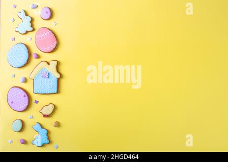 Frohe Ostern. Bunte Pastellkekse auf gelbem Hintergrund, verschiedene Lebkuchen glasiert, flach liegend, Blick von oben, Platz für Grußtext, Banner, Flyer, Gutschein. Stockfoto