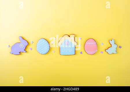 Frohe Ostern. Bunte Pastellkekse auf gelbem Hintergrund, verschiedene Lebkuchen glasiert, flach liegend, Blick von oben, Platz für Grußtext, Banner, Flyer, Gutschein. Stockfoto