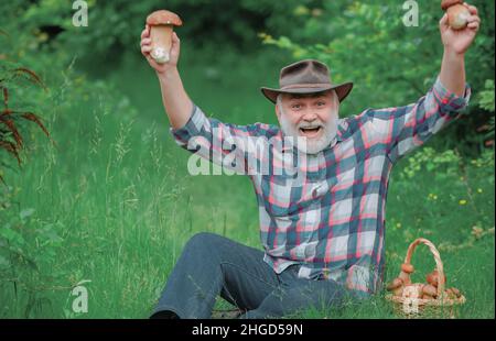 Großvater mit einem Korb von Pilzen und einem überraschenden Gesichtsausdruck. Glücklicher Großvater - Sommer und Hobbys. Alter Mann zu Fuß - Pensionszeit. Stockfoto