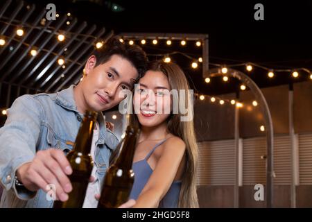 Glücklich asiatische Teenager Paar Mann und Frau verliebt Bier Alkohol trinken und Toasting Flasche in der Feier Partei. Junge glückliche Paar Liebe und romantisch Stockfoto