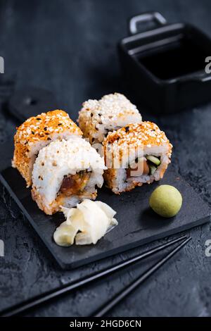 Verschiedene Sushi-Rollen auf dunklem Hintergrund mit Essstäbchen, Wasabi und Sojasauce. Traditionelles japanisches Street Food Stockfoto