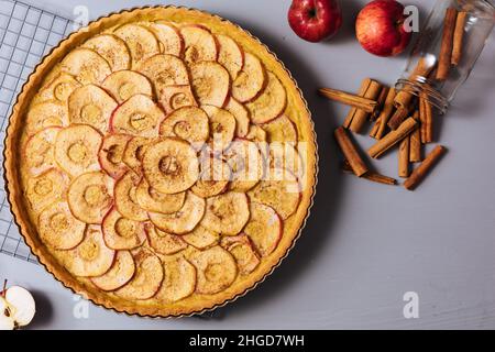 Draufsicht auf klassische französische Apfeltarte auf grauem Hintergrund mit Äpfeln und Zimtstangen Stockfoto