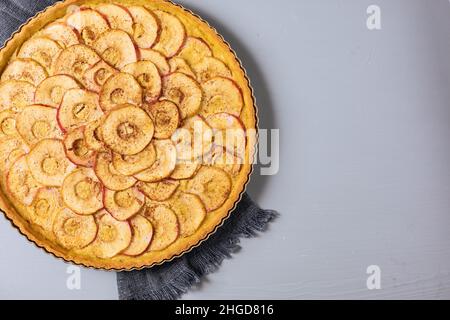 Draufsicht auf klassische französische Apfeltarte auf grauem Hintergrund mit Äpfeln und Zimtstangen Stockfoto