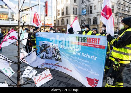 29. Dezember 2021, Sachsen-Anhalt, Halle (Saale): Demonstrierende Feuerwehrleute in Profikleidung stehen mit Banner und Ver.di-Fahnen vor dem Ratshof. Vor ihnen ist ein verbrannter Weihnachtsbaum mit formulierten Forderungen. Sie protestieren gegen „geheime Kostensenkungsmaßnahmen“ und mangelnde Wertschätzung. Foto: Kevin Meyer/dpa-Zentralbild/dpa Stockfoto