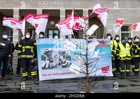 29. Dezember 2021, Sachsen-Anhalt, Halle (Saale): Demonstrierende Feuerwehrleute in Profikleidung stehen mit Banner und Ver.di-Fahnen vor dem Ratshof. Vor ihnen ist ein verbrannter Weihnachtsbaum mit formulierten Forderungen. Sie protestieren gegen „geheime Kostensenkungsmaßnahmen“ und mangelnde Wertschätzung. Foto: Kevin Meyer/dpa-Zentralbild/dpa Stockfoto