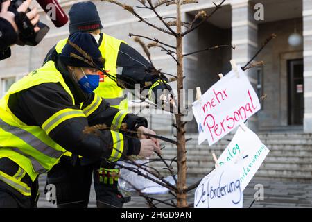 29. Dezember 2021, Sachsen-Anhalt, Halle (Saale): Zwei Feuerwehrleute hängen in Uniform mit Forderungen an die Stadt an einen verbrannten Weihnachtsbaum vor dem Ratshof. Sie protestieren gegen „geheime Kostensenkungsmaßnahmen“ und mangelnde Wertschätzung. Foto: Kevin Meyer/dpa-Zentralbild/dpa Stockfoto