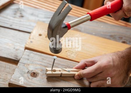 Männliche Hand halten Hammer und Nagel eine Wäscheklammer, Holz Arbeitstisch Hintergrund. DIY, Hausreparatur und Reparatur. Stockfoto