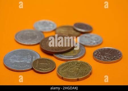 Münzen verschiedener Länder. Eine Streuung von Münzen auf dem orangen Hintergrund. Geringe Schärfentiefe, Kopierbereich Stockfoto