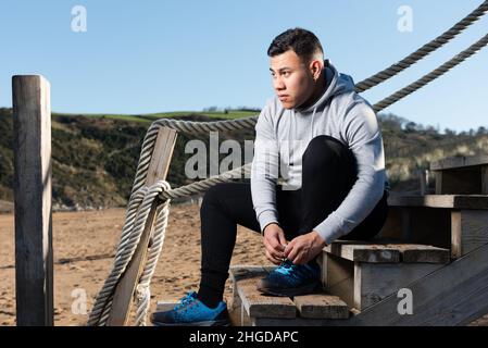 Lateinamerikanischer junger Läufer, der vor dem Training Schnürsenkel bindet. Stockfoto