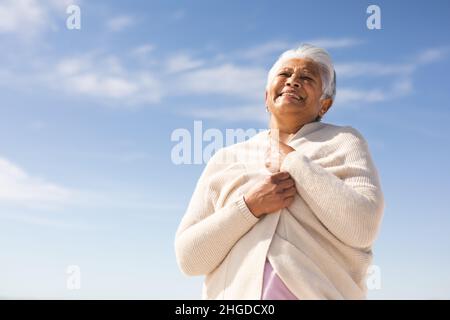 Blick aus der Ferne auf eine glückliche ältere Frau mit Achselzucken und Blick auf den Strand vor blauem Himmel Stockfoto