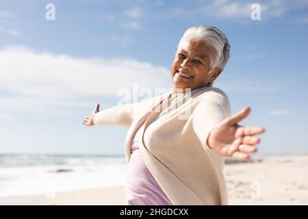 Porträt einer fröhlichen älteren Frau mit ausgestreckten Armen, die am sonnigen Strand in den Ruhestand geht Stockfoto
