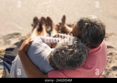 Blick aus dem hohen Winkel auf ein liebevolles, multirassisches Seniorenpaar, das einen sonnigen Tag am Strand genießt Stockfoto