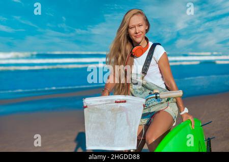 Junge Frau mit Surfbrett und Fahrrad am Strand. Stockfoto