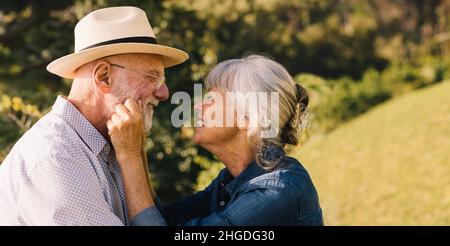 Ältere Paare lächeln einander mit Liebe und Zuneigung an. Grauhaarige Paare, die einen romantischen Moment im Park verbringen. Glücklicher Senior Coup Stockfoto