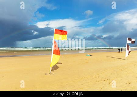 Ausgewiesene Badegebiete sind an den Stränden mit den roten und gelben Flaggen der RNLI gekennzeichnet. Diese Flaggen weisen auf Bereiche hin, die von Rettungsschwimmern überwacht werden. Im Design Stockfoto