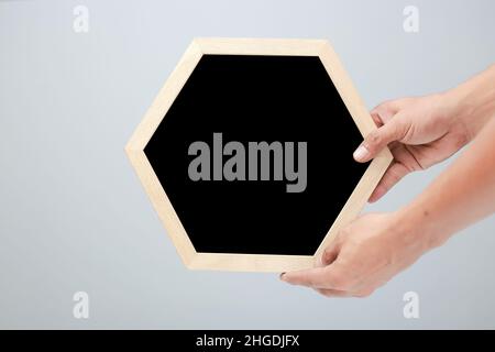 Herrenhänden mit leerem sechseckigem Rahmen in minimalistischem femininem Stil, unterstützt durch weichen grauen Leinenhintergrund – perfekt zum Schreiben von Begrüßungen. Flatfront Stockfoto