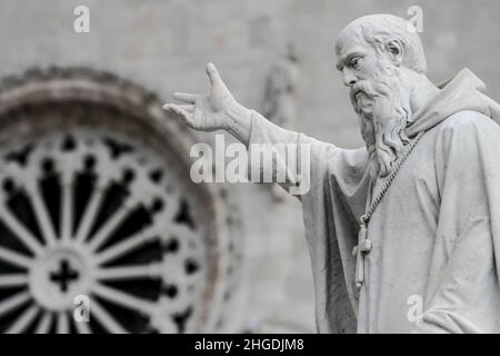 Die Kirche des heiligen Benedikt, gegenüber der Piazza San Benedetto. Die Statue von San Benedict im Vordergrund, Norcia, Umbrien, Italien Stockfoto