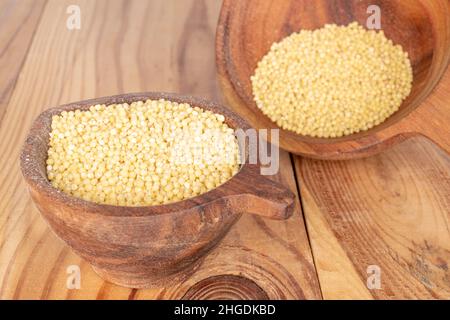 Trockene Bio-Hirse in zwei Holzbechern auf einem Holztisch. Stockfoto