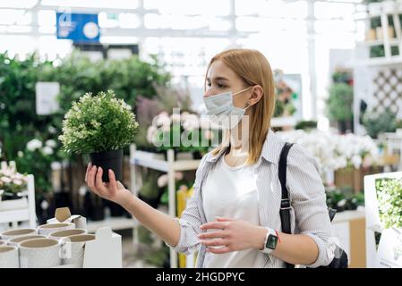 Aufnahme einer Frau mit Schutzmaske und Kauf von Pflanzen im Gartenladen während einer Coronavirus-Pandemie. Gartencenter. Stockfoto