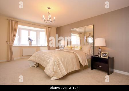 Hauptschlafzimmer in cremefarbenen neutralen Farben, beigefarbener Teppich, Kingsize-Doppelbett, Bettüberwurf, Spiegelkopfteil, Nachttischlampen, Erkerfenster. Stockfoto