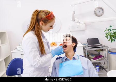 Hoher Winkel des männlichen Patienten Öffnung Mund und Blick auf weibliche Zahnärztin beim Besuch der zeitgenössischen Zahnklinik für Check-up Stockfoto